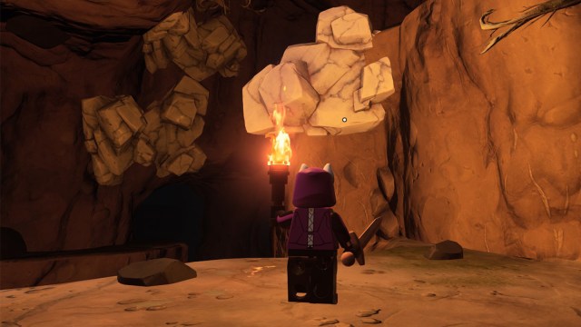 A LEGO Fortnite character holding a torch, looking at a cluser of marble stuck to the wall of a cave.