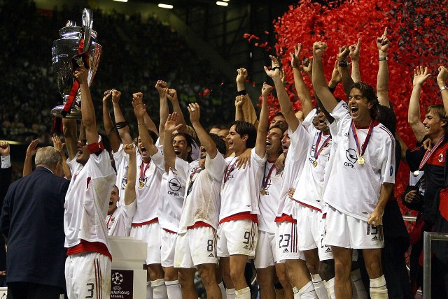 AC Milan players, wearing a white kit, lifting the Champions League trophy as red confetti falls. 