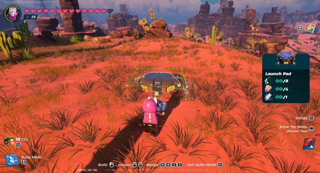 A LEGO Fortnite character, wearing a pink hoodie, placing down a Launch Pad in the desert. 